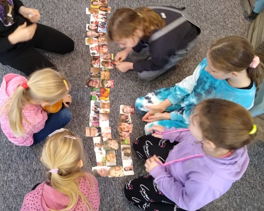 Zdjęcie przedstawia dzieci siedzące na dywanie nad kartami przedstawiającymi ludzkie emocje